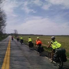 6 people in neon jackets riding on a long country road