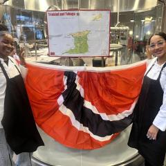 Two students in chef jackets hold a Trinidadian flag