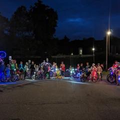 30 people with bikes and lots of colorful lights on their bikes standing in a parking area at night