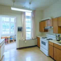 A communal kitchen with a stove, oven, sink, fridge, countertops, cabinets, a table, and chairs.