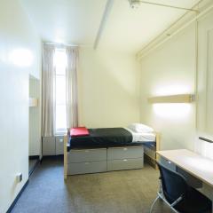 A bedroom with a twin bed, desk, dresser, chair, and lamp.