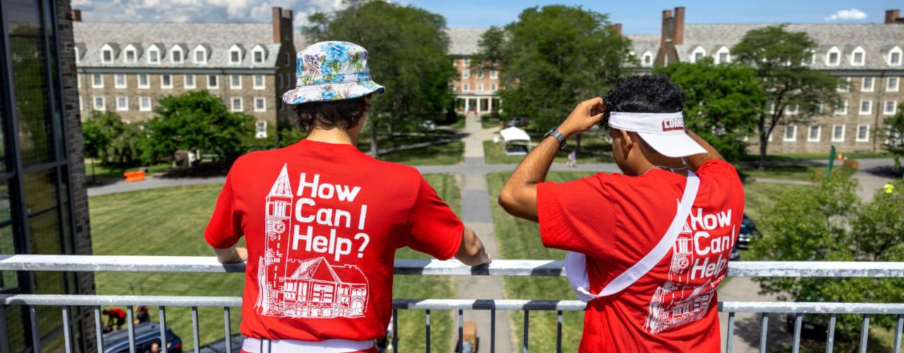 Move-in day 2022, "How Can I Help" featured on the back of the shirts of two staff members looking out across campus.