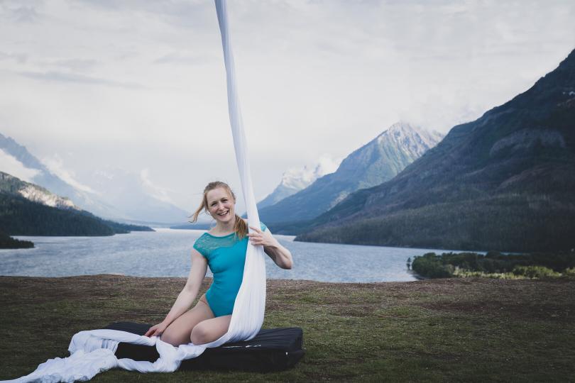 aerial silks hanging with woman in blue leotard seated next to them a base of a lake in mountainscape