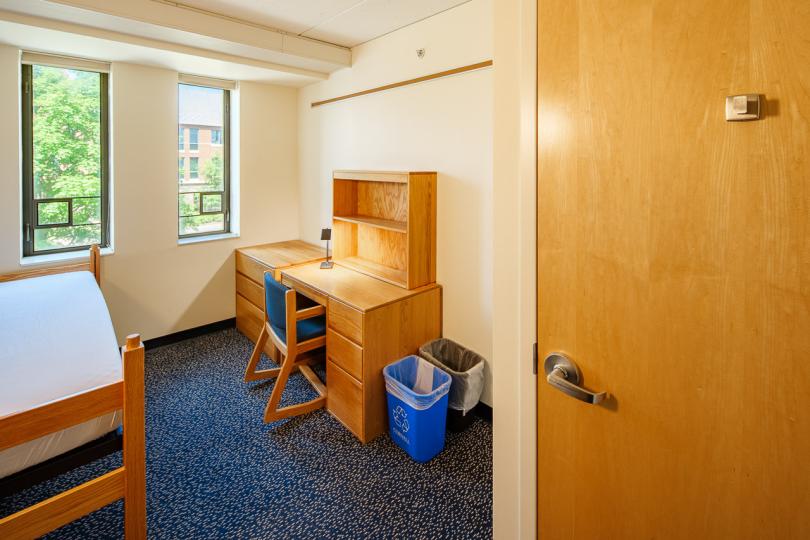 Single room in Mews Hall with a twin bed, desk, chair, lamp, dresser, and window.