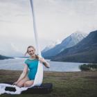 aerial silks hanging with woman in blue leotard seated next to them a base of a lake in mountainscape