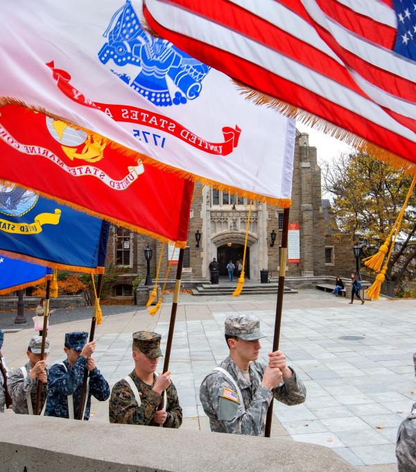 Military personnel holding flags with cloudy sky background.