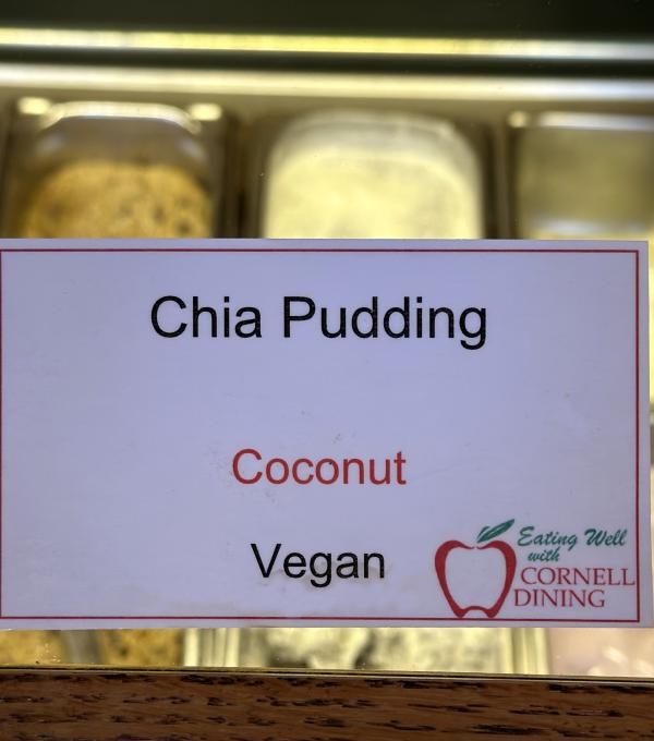 Chia Pudding menu identifier card with coconut allergen labeled and food bins beyond it