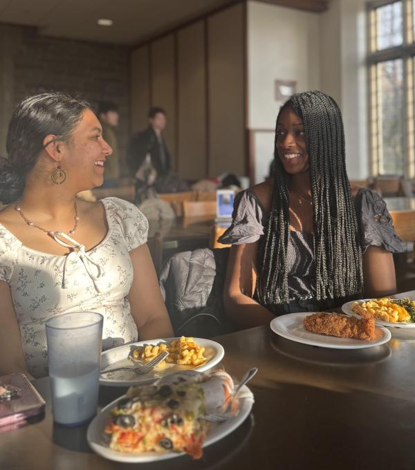 Students smile at each other at a table with plates of food in front of them