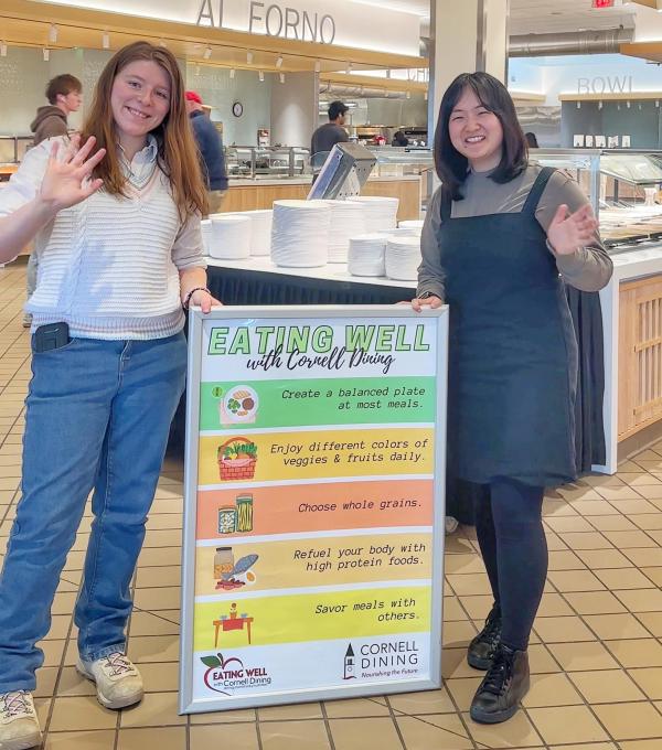 Students hold a sign that says Eating Well with Cornell Dining with a list of tips