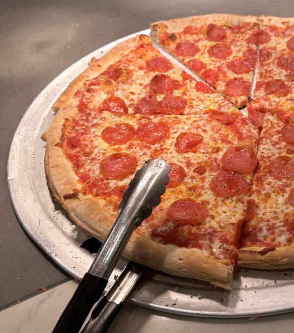 Tongs reach for a slice of pizza out of a pepperoni pizza resting on a pan