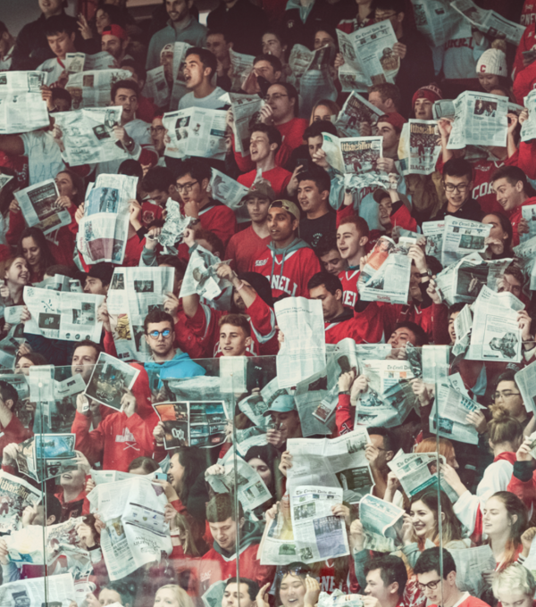 Students at a hockey game with newspapers chanting