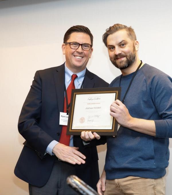 Two people on stage, one holding an award certificate