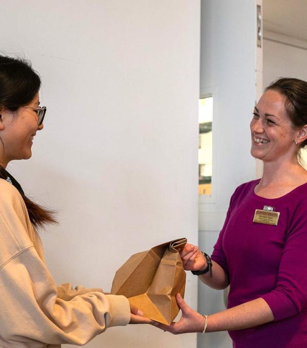 A smiling Dining staff member hands a bagged meal to a student