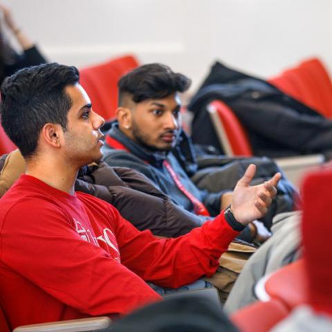 Two male students talking to group during 1vyG conference