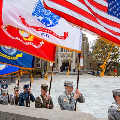 Military personnel holding flags with cloudy sky background.