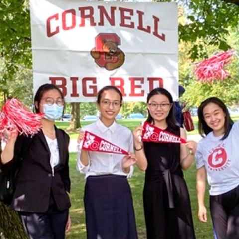 Angela Pan ’23, right, stands with three friends on campus in front of BIG RED CORNELL sign and waving red Cornell pinnies during Homecoming 2021
