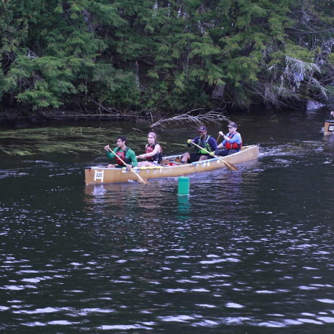 Students paddle two canoes down a waterway, greenery in the background.