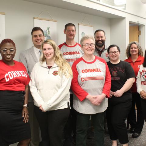 Nine members of the Office of Student Conduct and Community Standards pose for a group photo in front of a white wall wearing red Cornell gear.