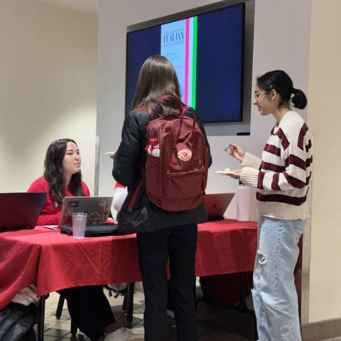 Students sit at a table, with more students standing in front holding plates