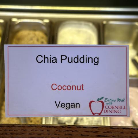 Chia Pudding menu identifier card with coconut allergen labeled and food bins beyond it