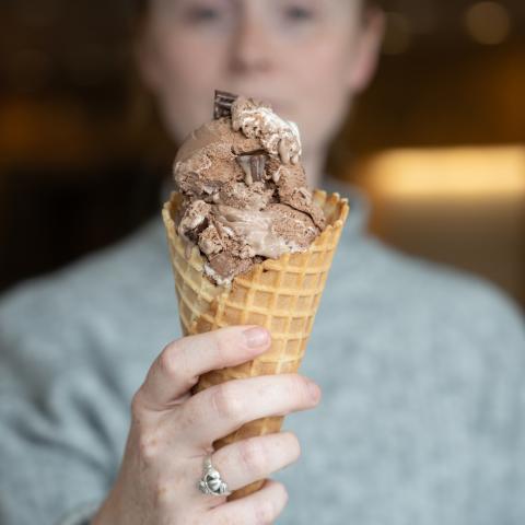 A closeup of an ice cream cone in the foreground held by a person who's blurred in the background
