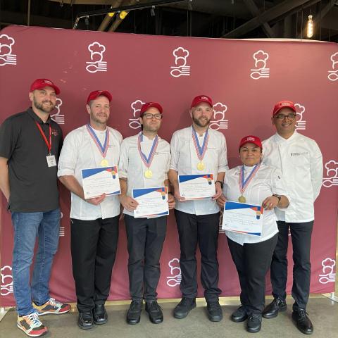 A row of smiling people wearing chef coats and caps hold certificates