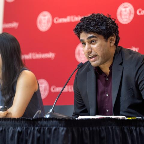 Students in front on red Cornell banner; one speaks into a microphone