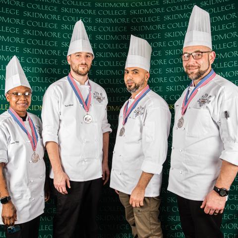 Four people in chef jackets and toques each wearing a silver medal