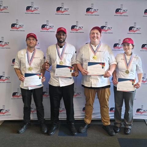 Four chefs smiling with gold medals and certificates