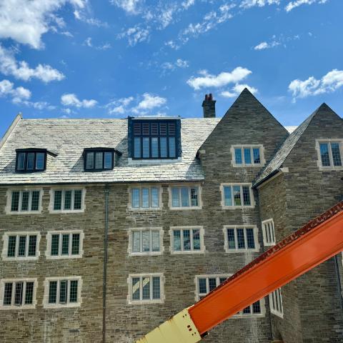 An old-fashioned stone college building with slate tiled roof, and a crane arm extending across the view