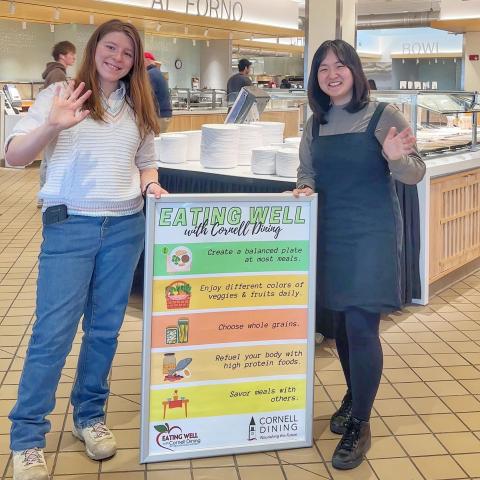 Students hold a sign that says Eating Well with Cornell Dining with a list of tips