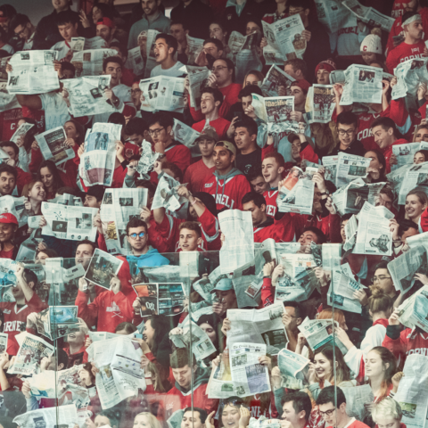 Students at a hockey game with newspapers chanting