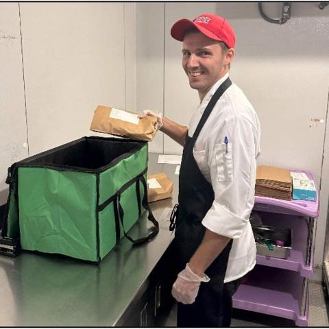 A smiling person in an apron places a paper-wrapped item in a large open cooler