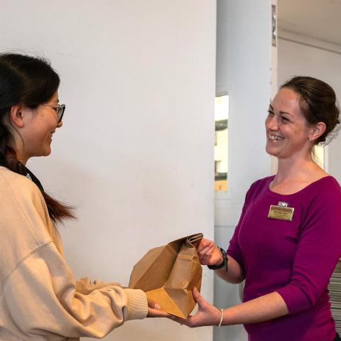 A smiling Dining staff member hands a bagged meal to a student