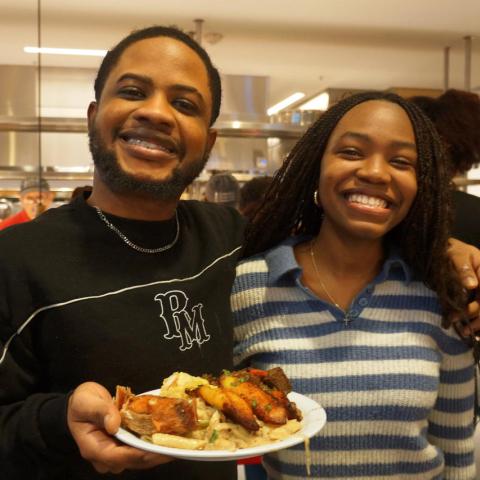 Two Black people smiling, with one holding a plate of food
