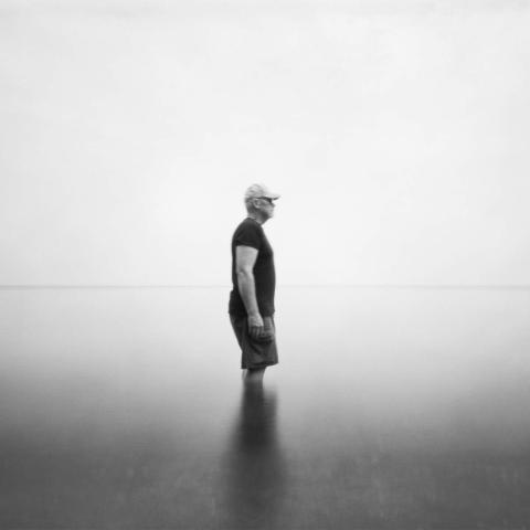 A person stands in a lake facing to the side in a black and white photo
