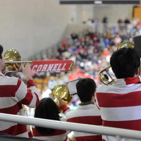 Several band members seen from behind, wearing red and white stripes, with fans in the stands in the background