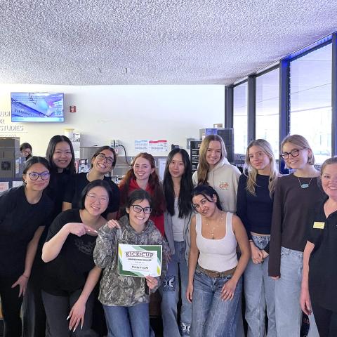 About a dozen people stand in two rows, with one holding a certificate that says Kick the Cup