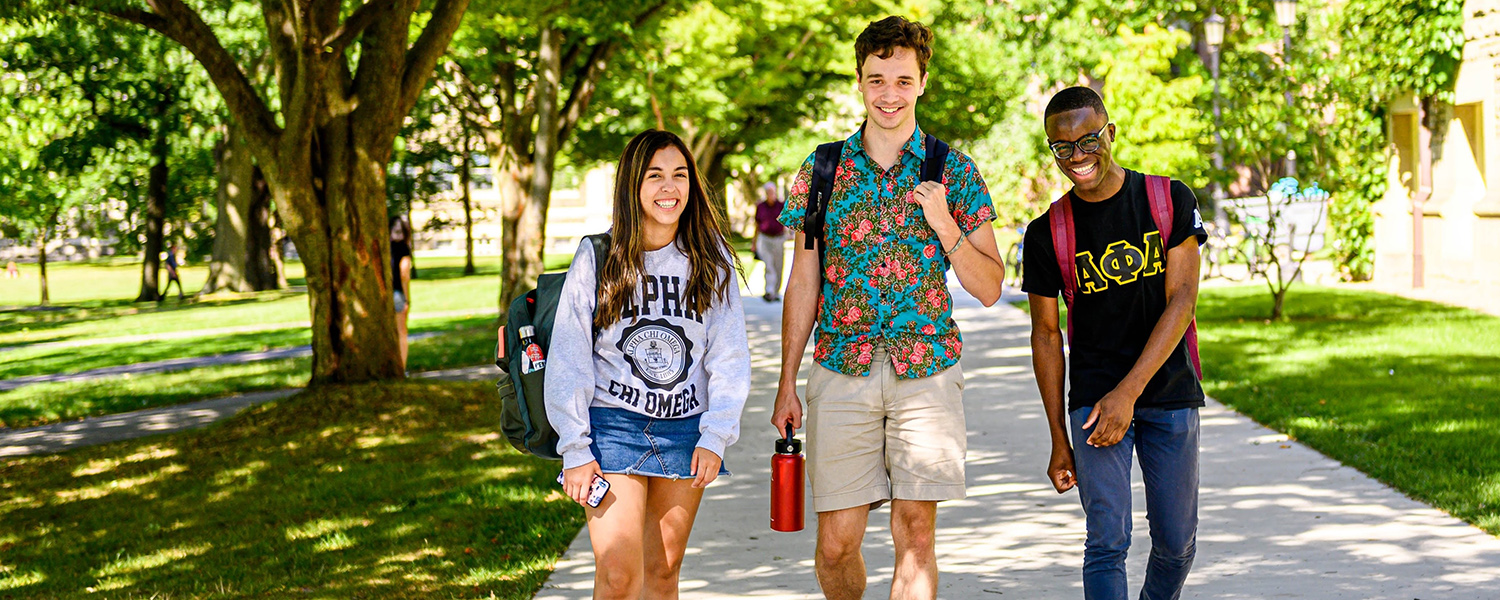 Three students walking in Arts Quad wearing Greek letter clothing