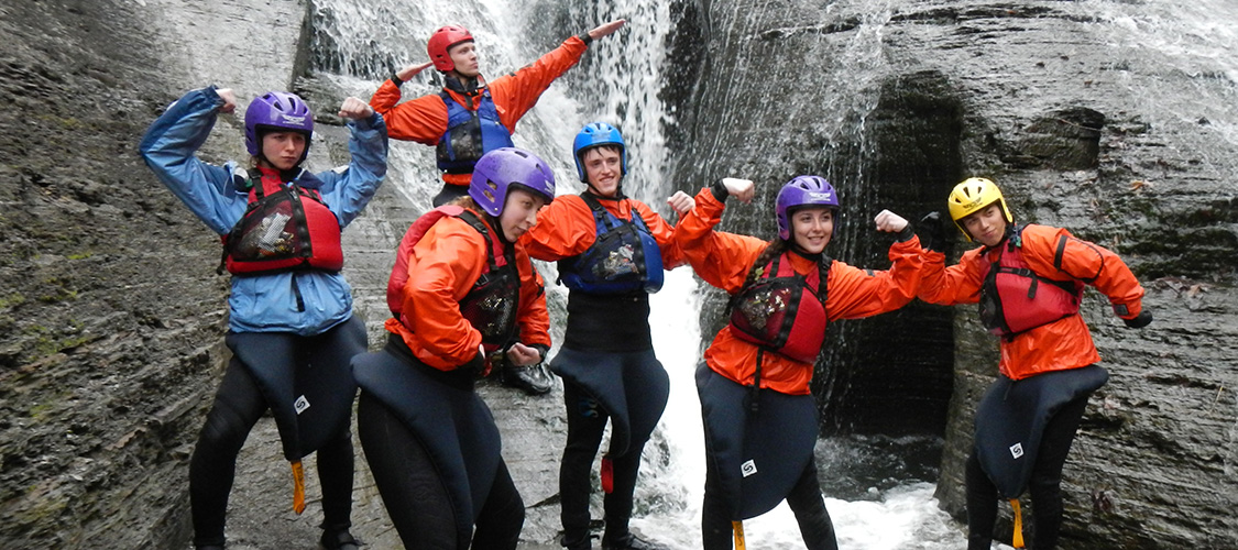 Whitewater kayaking students show their best hero pose in front of a waterfall
