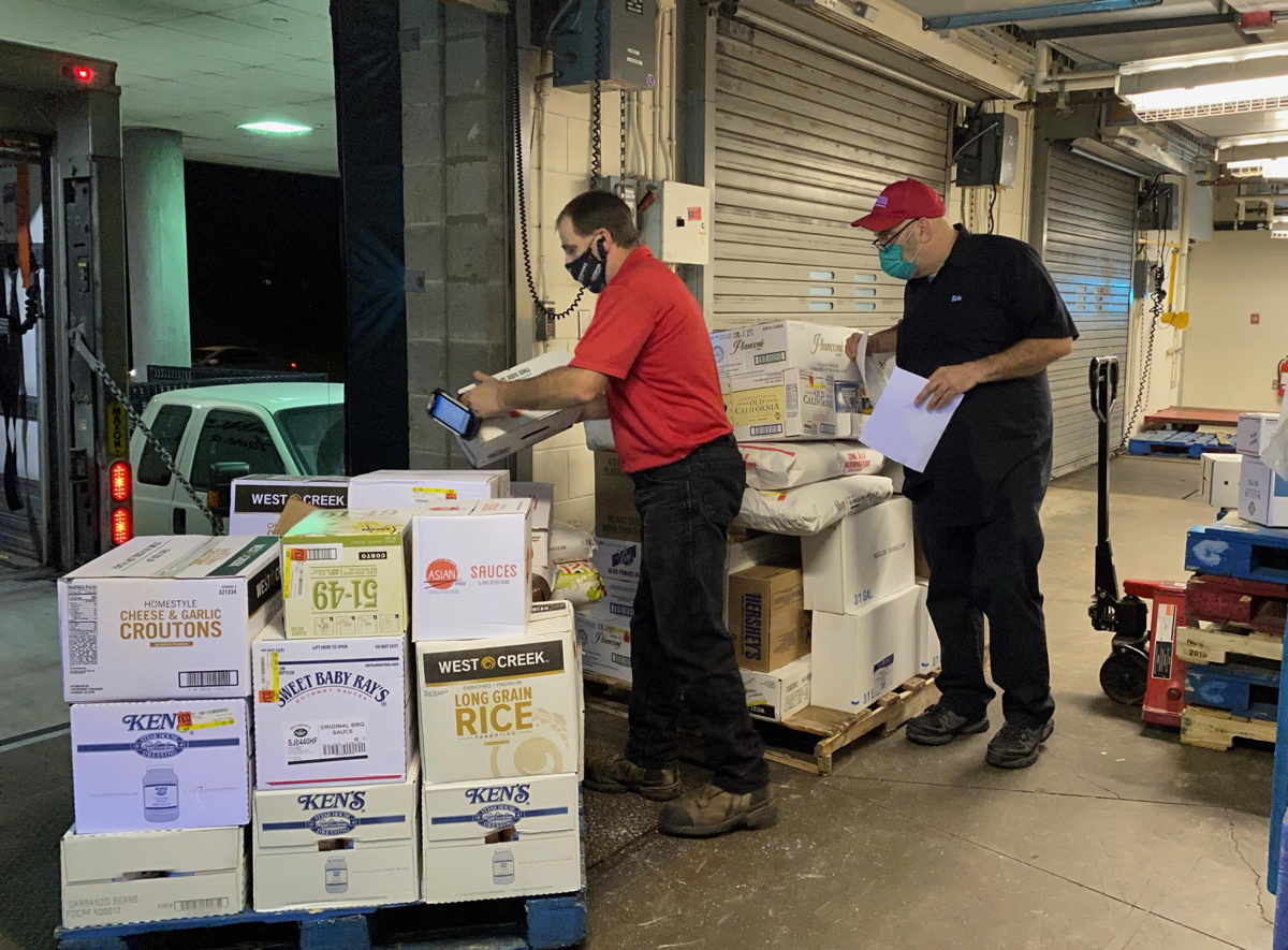 Two people unload a pallet of food supplies at a loading dock