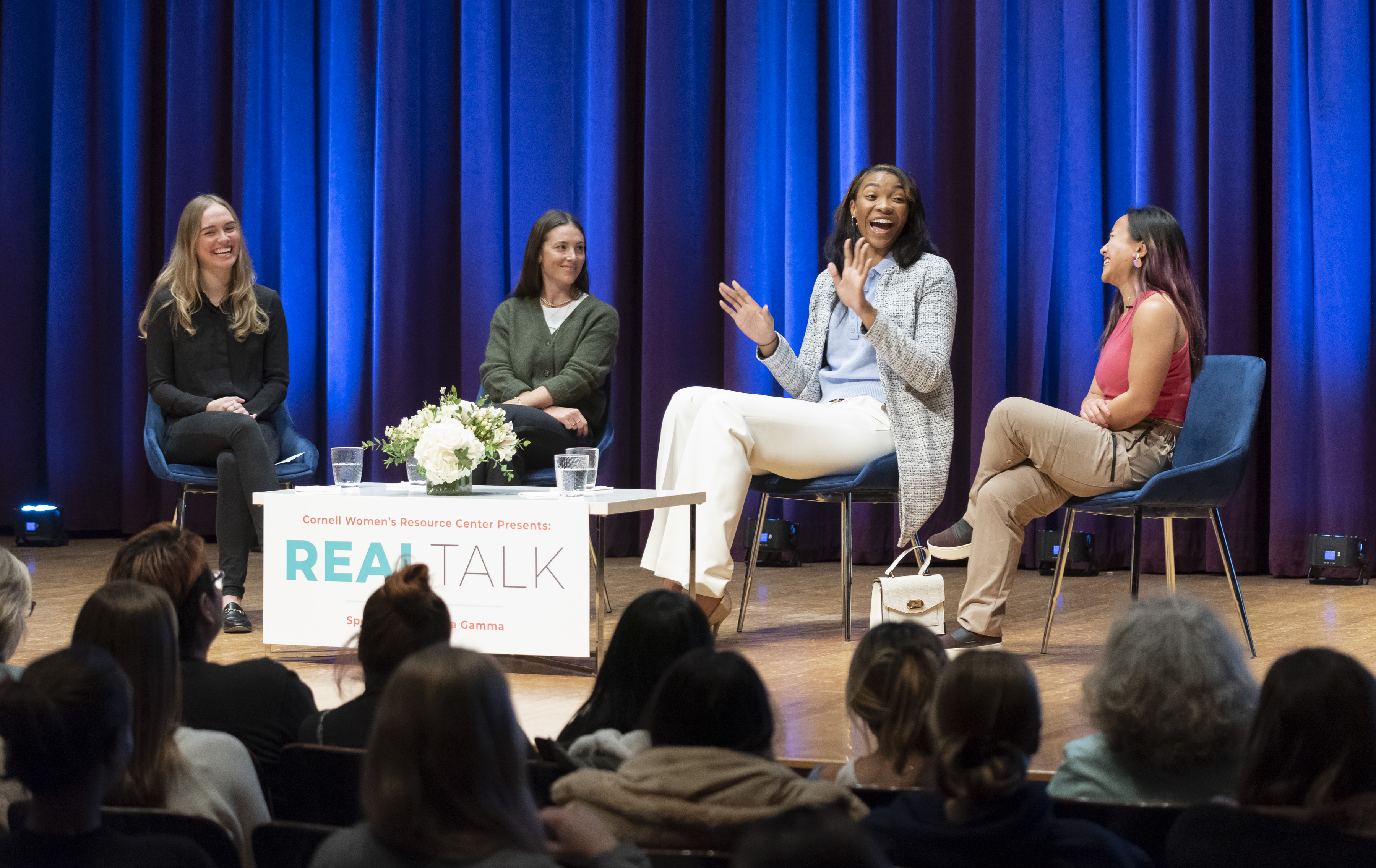 Four women sit onstage in front of an audience.
