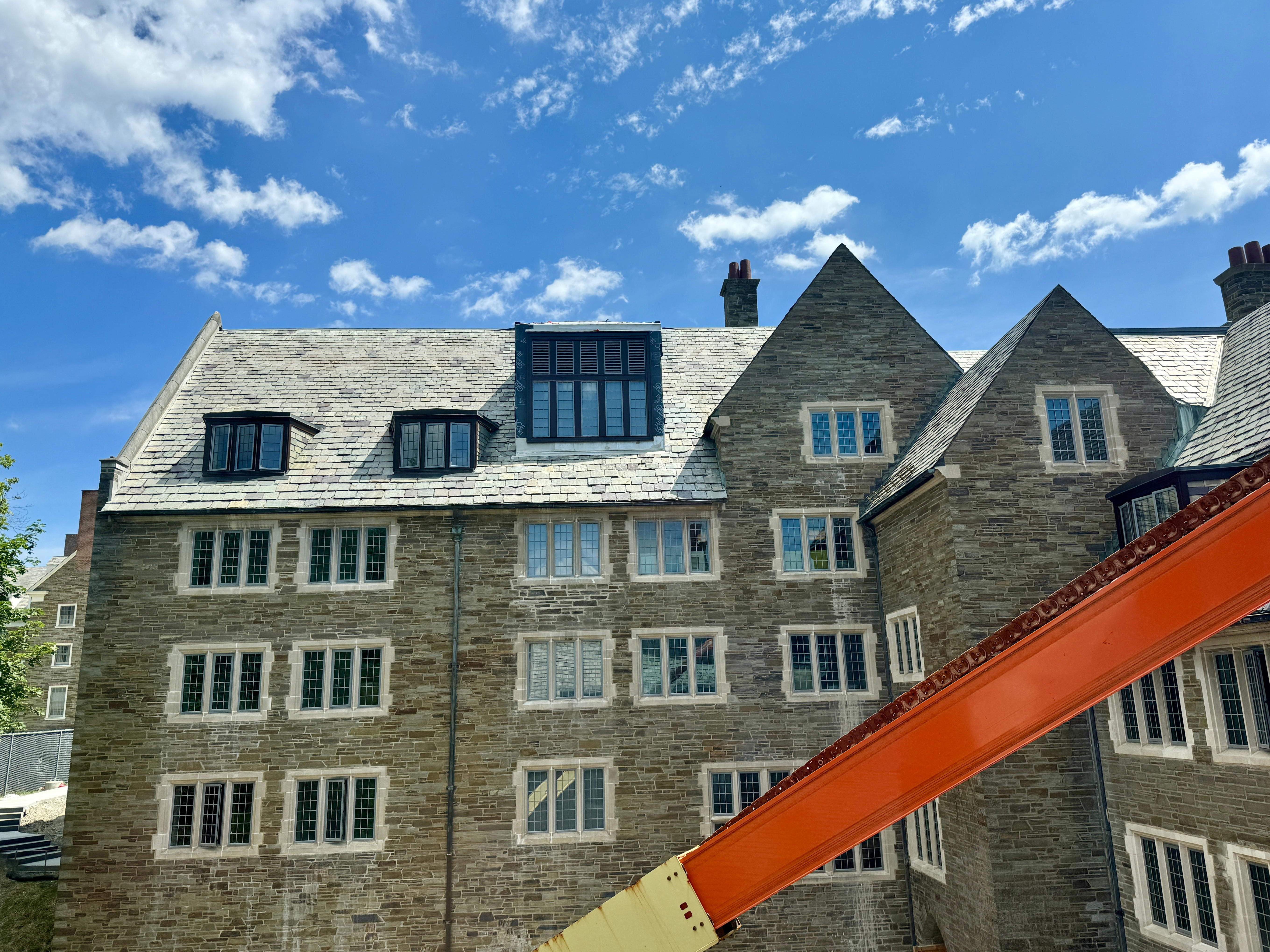 An old-fashioned stone college building with slate tiled roof, and a crane arm extending across the view