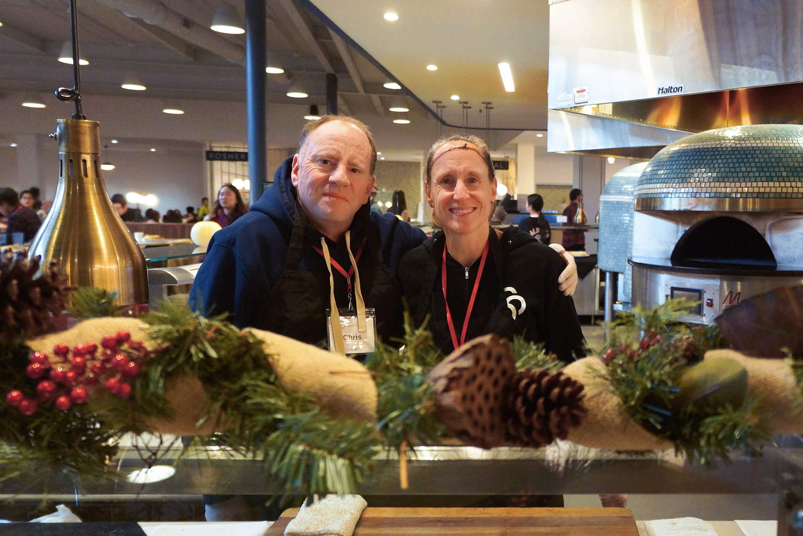 Two volunteers stand behind a counter decorated with pinecones and gourds