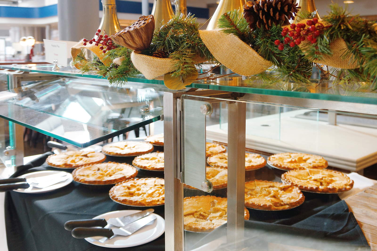 A serving counter with several pies, decorated above with pinecones and evergreen boughs
