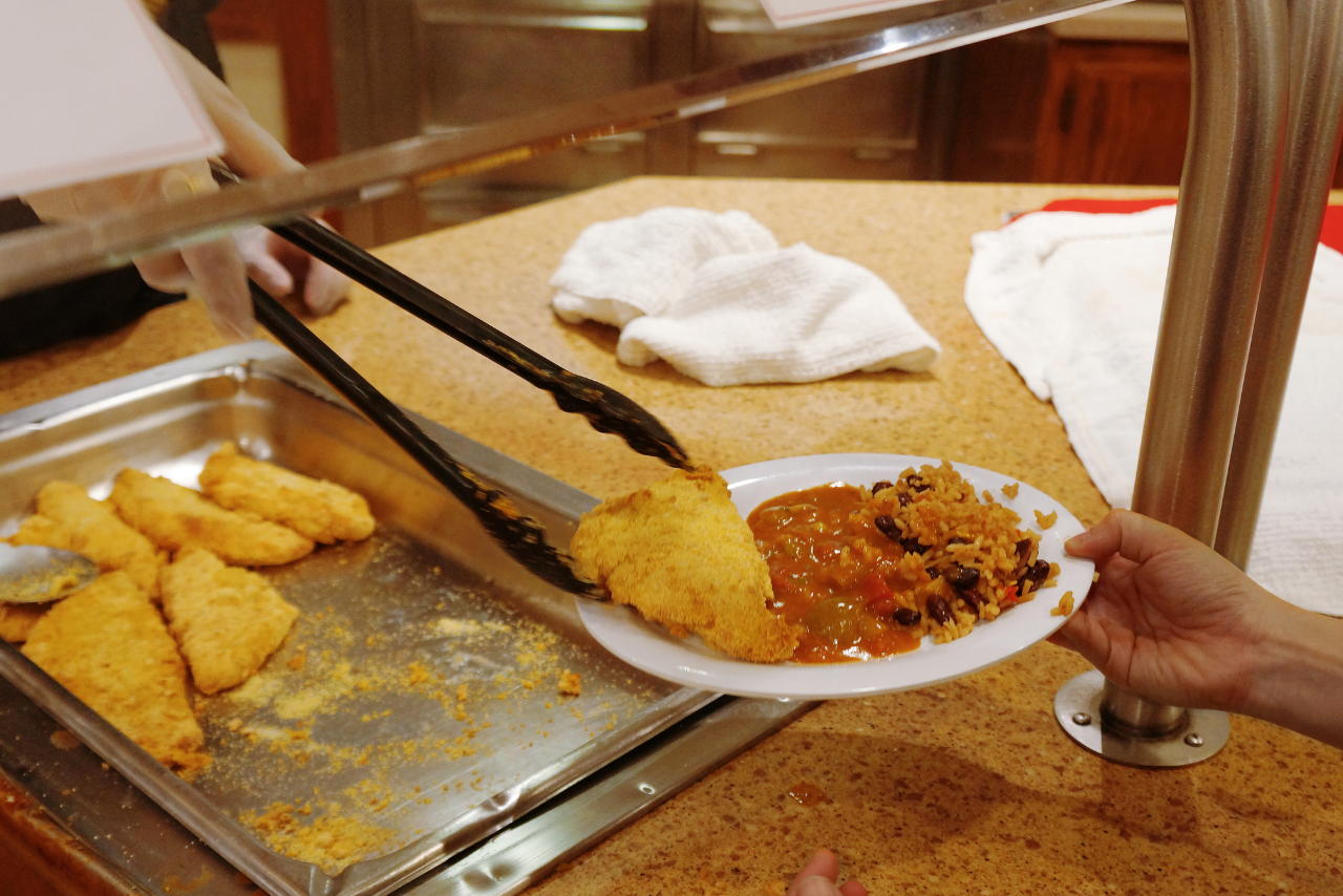 A closeup of a hand with tongs serving food onto a plate