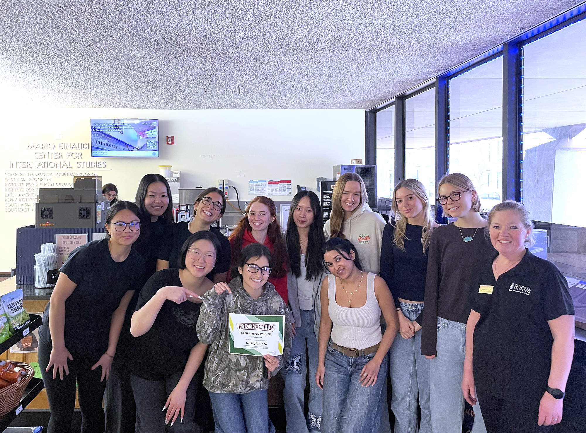 About a dozen people stand in two rows, with one holding a certificate that says Kick the Cup