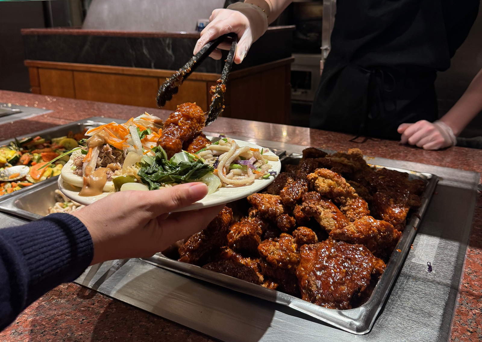 A person behind a serving line serves food onto a plate being held by a guest