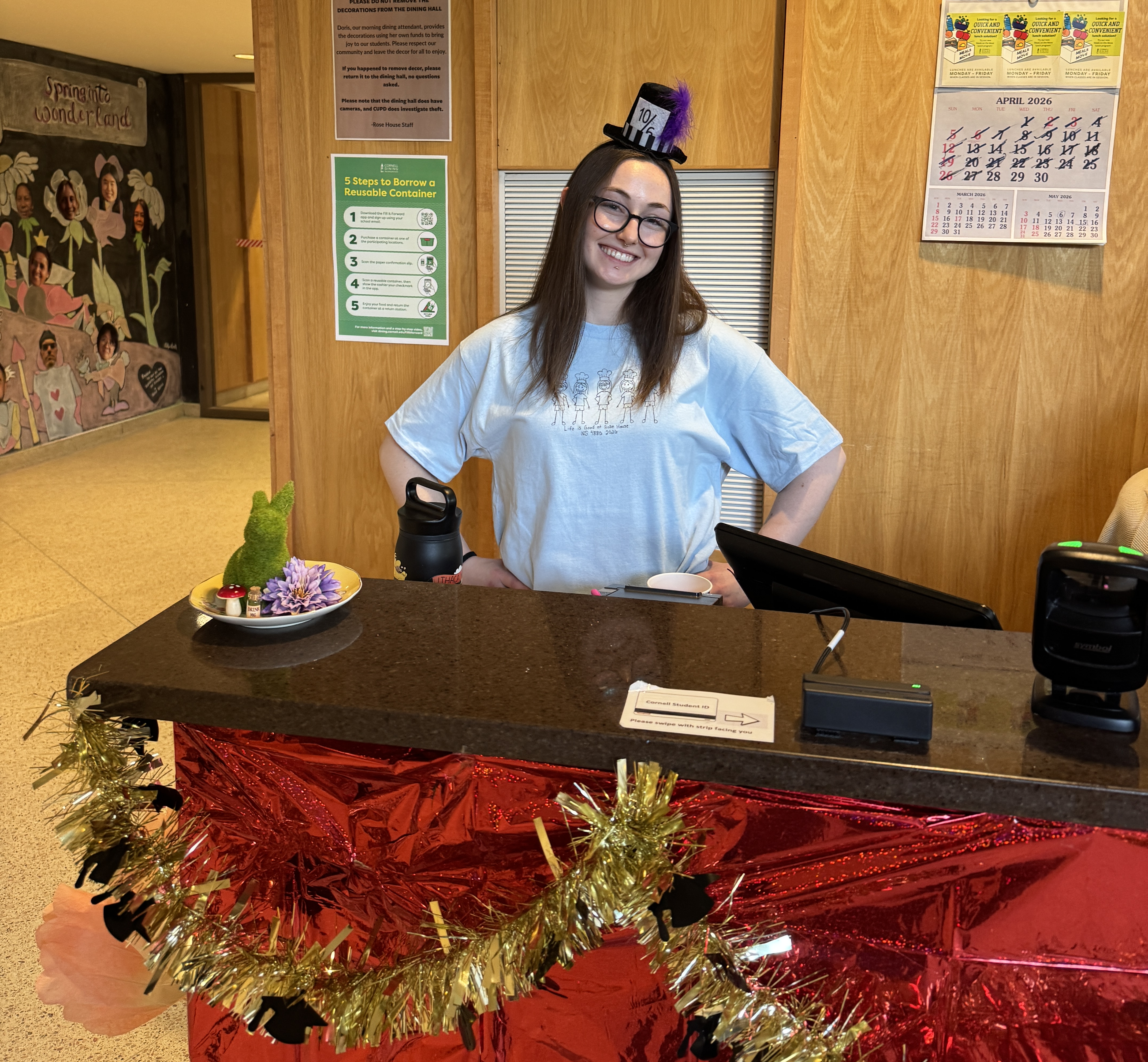 A person wearing a jaunty small hat stands at the dining room front desk