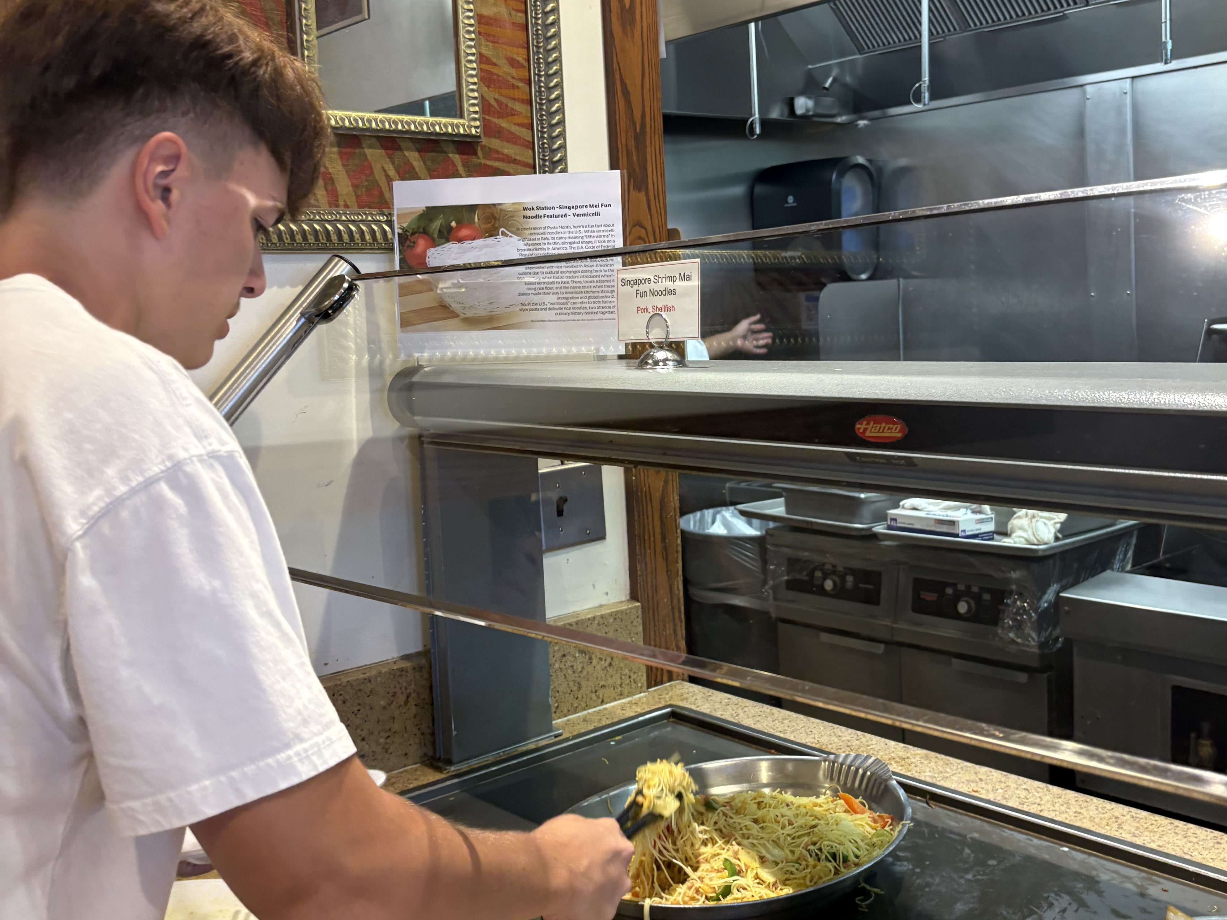 A person serves himself food from a serving dish of noodles